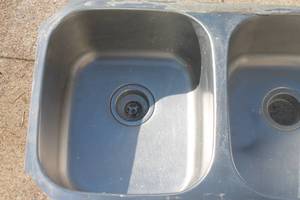 Stainless steel double-basin undermount kitchen sink showing light surface wear and residue around the rim.