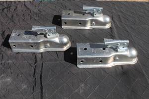 lot 7 image: Set of three galvanized steel trailer couplers with lever-locking mechanisms, showing light surface wear.
