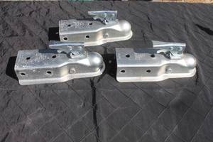 lot 8 image: Set of three galvanized steel trailer couplers with lever-locking mechanisms, showing light surface wear.
