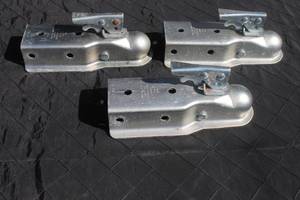 lot 9 image: Set of three galvanized steel trailer couplers with lever-locking mechanisms, showing light surface wear.
