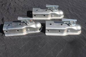 lot 10 image: Set of three galvanized steel trailer couplers with lever-locking mechanisms, showing light surface wear.