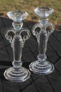 lot 21 image: Pair of vintage clear pressed glass candlesticks with decorative curved side handles and stepped octagonal bases.