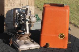 lot 23 image: Vintage Revere Model 85 8mm movie projector in a hammered metallic finish, complete with its original textured orange carrying case.