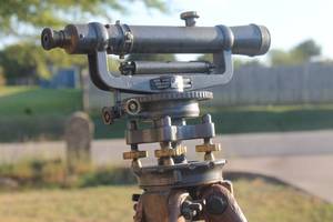 lot 24 image: Vintage David White Instrument Company surveyor transit level mounted on a wooden tripod, featuring brass adjustment knobs and aged patina.