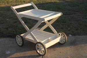 lot 29 image: White painted wooden outdoor bar cart featuring a two-tiered slatted design, built-in bottle holders, and four spoke wheels.