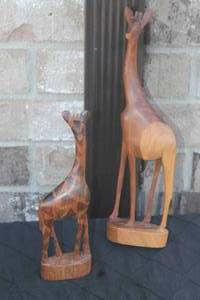 lot 42 image: Pair of hand-carved wooden giraffe statues, featuring one with detailed geometric spot carvings and one smooth-finished stylized figure.